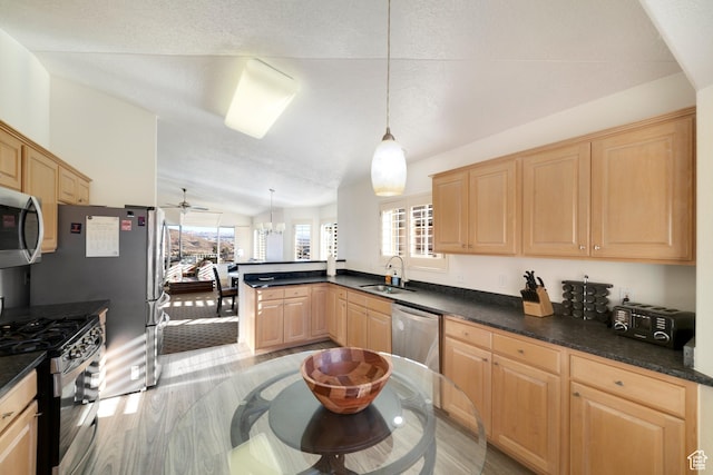 kitchen featuring stainless steel appliances, light wood-style floors, a sink, dark countertops, and vaulted ceiling