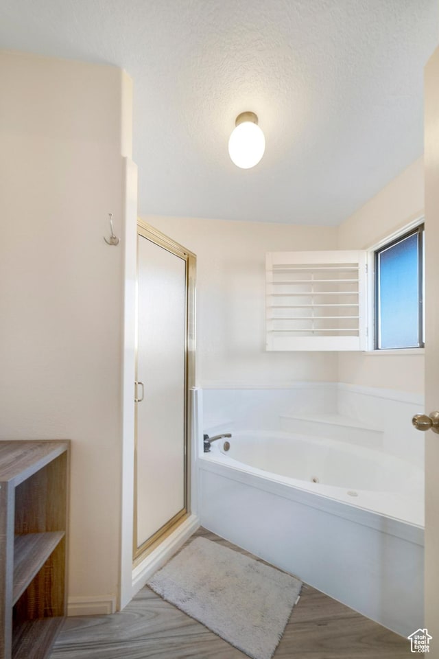 full bath featuring a bath, a stall shower, wood finished floors, and a textured ceiling