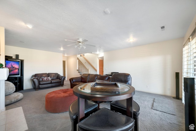 living room featuring carpet floors, a ceiling fan, and stairs