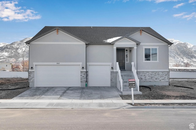 view of front of home with driveway, an attached garage, stucco siding, stone siding, and a mountain view