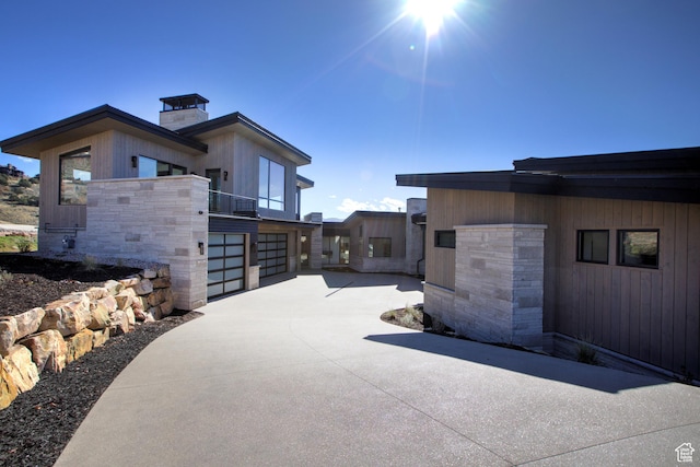 2066 E Oquirrh Mountain Cir, Heber City, UT 84032 - view of property exterior with driveway, stone siding, a garage, a balcony, and a chimney