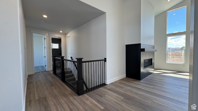 corridor featuring an upstairs landing, wood finished floors, recessed lighting, baseboards, and a towering ceiling