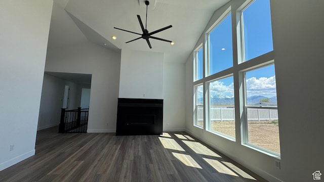 unfurnished living room with high vaulted ceiling, plenty of natural light, wood finished floors, and baseboards