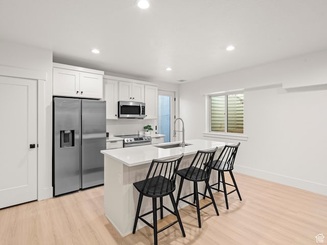 9749 N Hibiscus Ln, Eagle Mountain, UT 84005 - kitchen featuring stainless steel appliances, a sink, a kitchen island with sink, a breakfast bar area, and light wood-style flooring