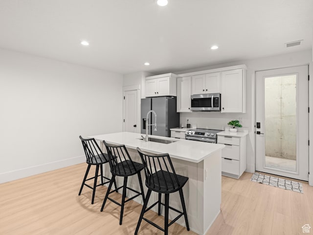 9749 N Hibiscus Ln, Eagle Mountain, UT 84005 - kitchen with stainless steel appliances, a sink, light wood-style flooring, a kitchen bar, and an island with sink