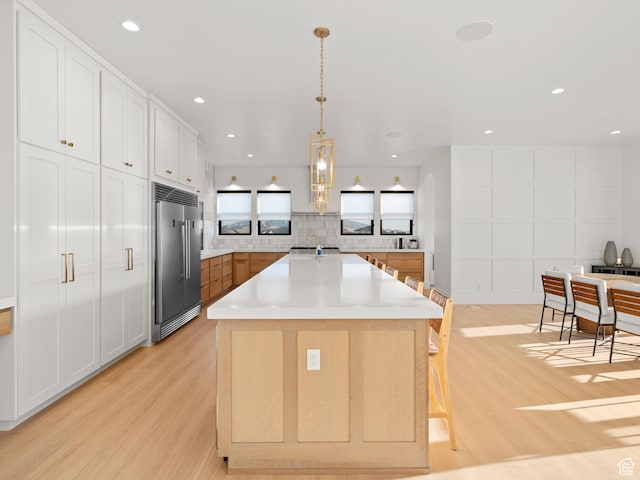 9749 N Hibiscus Ln, Eagle Mountain, UT 84005 - kitchen with built in refrigerator, a sink, light wood-style floors, light countertops, and an island with sink
