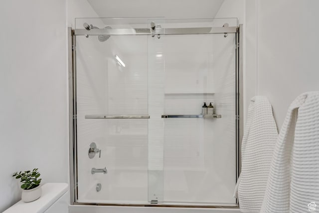 bathroom featuring toilet and shower / bath combination with glass door