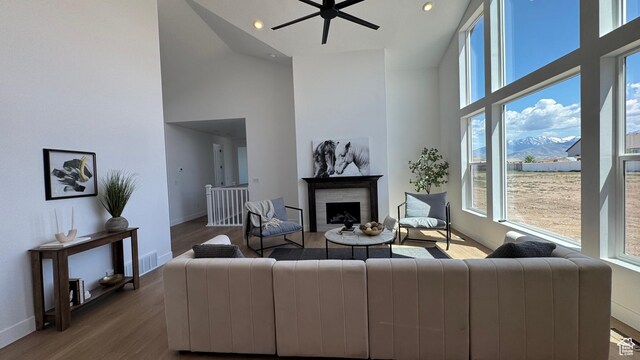 living room with high vaulted ceiling, plenty of natural light, a fireplace, wood finished floors, and ceiling fan