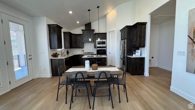 kitchen featuring appliances with stainless steel finishes, light countertops, a sink, light wood-type flooring, and vaulted ceiling
