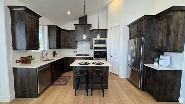 kitchen with appliances with stainless steel finishes, a sink, a center island, light wood-style floors, and vaulted ceiling