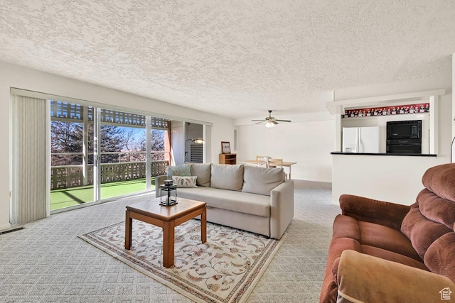 living area featuring carpet, ceiling fan, and a textured ceiling