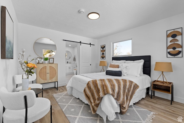 2386 E Lakeview Dr S, Millcreek, UT 84109 - bedroom with ensuite bathroom, a barn door, a textured ceiling, and light wood-type flooring