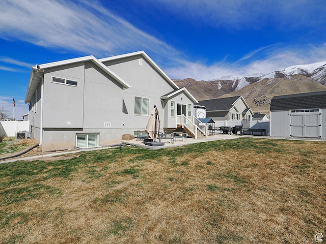 back of house featuring fence, a storage shed, a patio area, a mountain view, and an outbuilding
