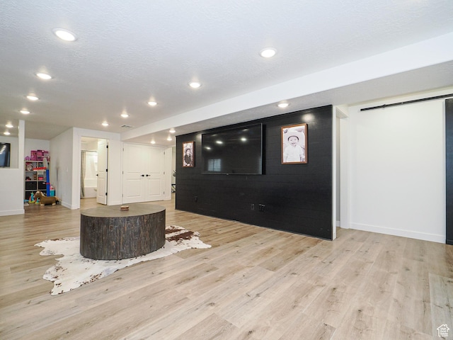 unfurnished living room featuring a barn door, light wood-style flooring, recessed lighting, and a textured ceiling