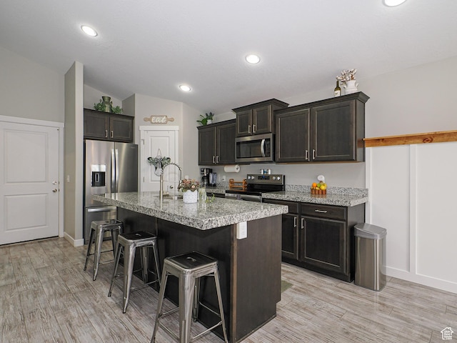 kitchen with a breakfast bar area, an island with sink, lofted ceiling, light wood-style flooring, and appliances with stainless steel finishes