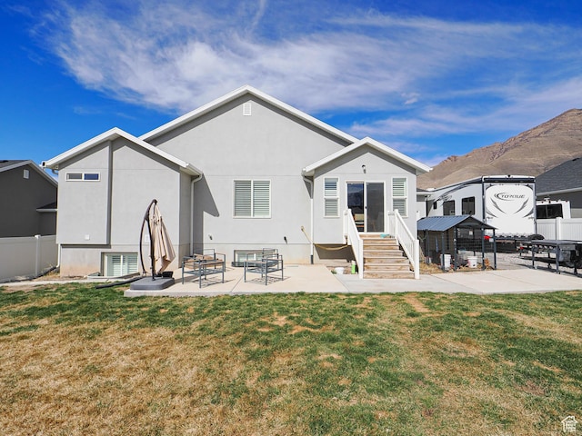 rear view of property with stucco siding, a lawn, a patio, and fence