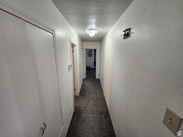 hall featuring a textured ceiling and dark colored carpet