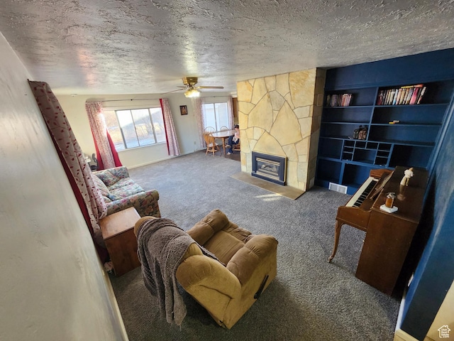 living room with ceiling fan, a stone fireplace, carpet floors, and a textured ceiling
