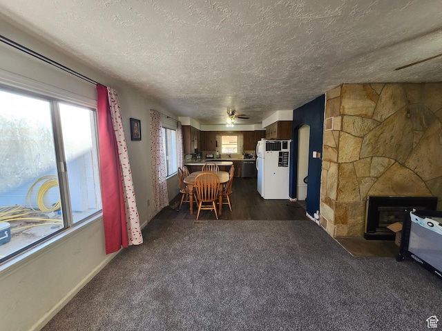 interior space featuring a stone fireplace, a healthy amount of sunlight, white fridge, and dark carpet