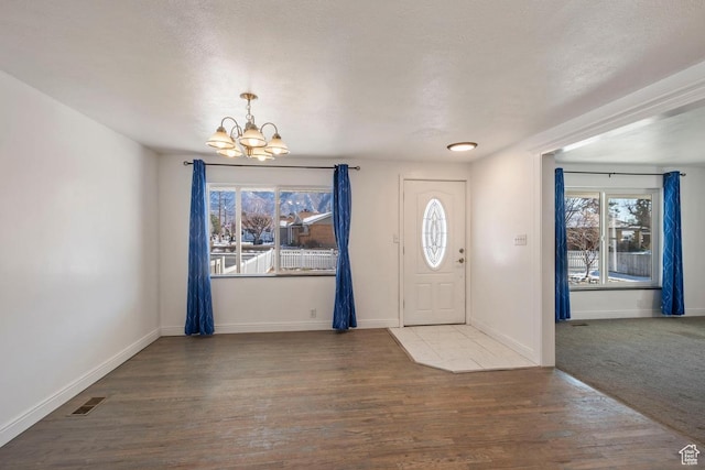 entrance foyer with visible vents, baseboards, an inviting chandelier, and wood finished floors
