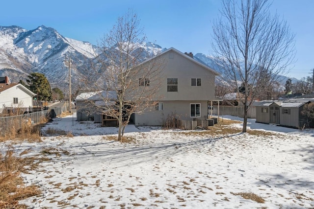 snow covered back of property with stucco siding, fence, an outdoor structure, and a shed