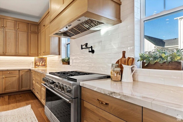 kitchen featuring hardwood / wood-style floors, decorative backsplash, stainless steel range, light stone countertops, and custom range hood