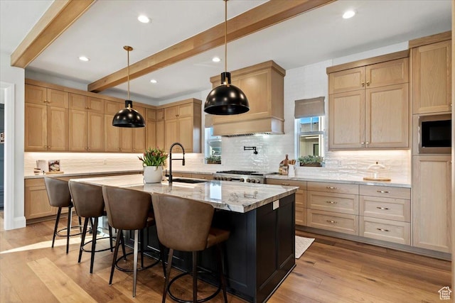 kitchen featuring pendant lighting, light brown cabinetry, sink, a kitchen island with sink, and beam ceiling