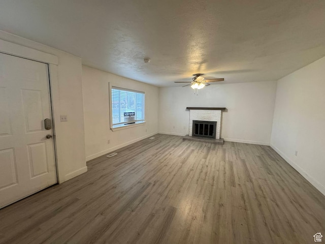 unfurnished living room with hardwood / wood-style floors, a fireplace, a textured ceiling, and ceiling fan