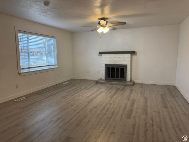 unfurnished living room featuring a brick fireplace, wood-type flooring, and ceiling fan
