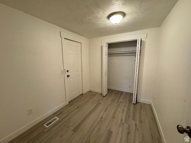unfurnished bedroom with a closet, a textured ceiling, and light hardwood / wood-style flooring