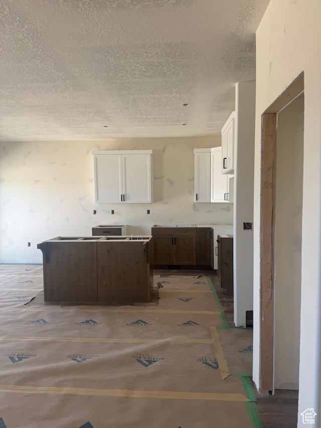 kitchen featuring a sink, a center island, a textured ceiling, and white cabinetry