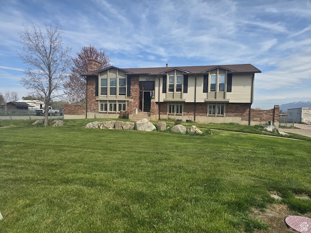 bi-level home with brick siding, entry steps, a chimney, and a front lawn