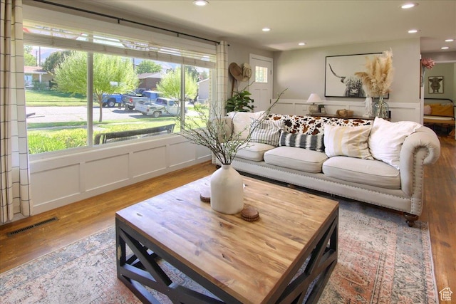 living area with wood finished floors, a wainscoted wall, visible vents, recessed lighting, and a decorative wall