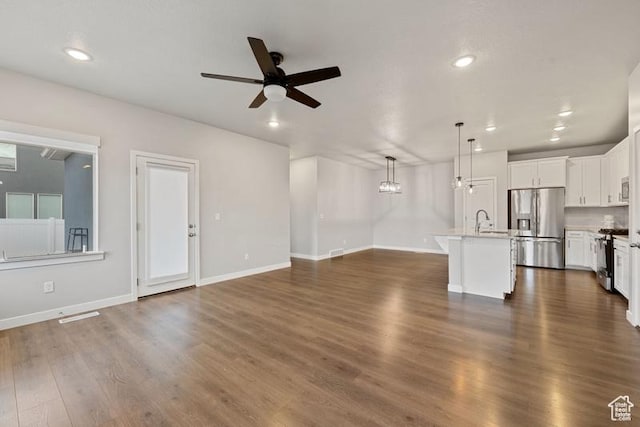 unfurnished living room with dark wood-style flooring, a sink, a ceiling fan, and baseboards