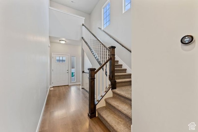 entryway with a high ceiling, wood finished floors, baseboards, and stairs