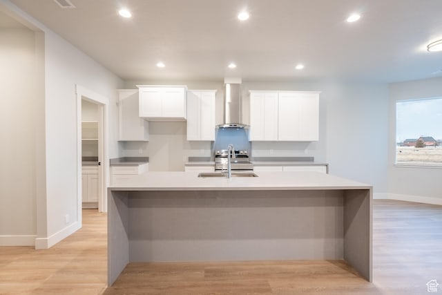 kitchen with light hardwood / wood-style flooring, wall chimney exhaust hood, a spacious island, sink, and white cabinetry