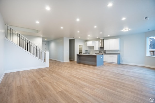 kitchen featuring white cabinetry, a kitchen island with sink, light hardwood / wood-style floors, sink, and wall chimney exhaust hood