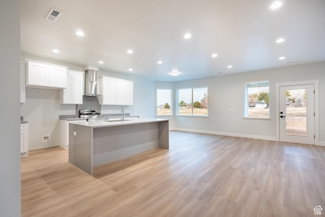 kitchen featuring white cabinetry, a center island with sink, light hardwood / wood-style flooring, stainless steel range oven, and wall chimney exhaust hood