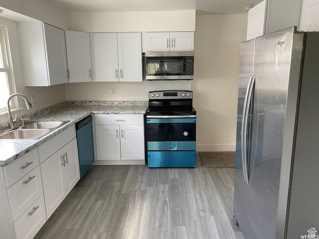 kitchen with sink, stainless steel appliances, light stone counters, white cabinets, and light wood-type flooring