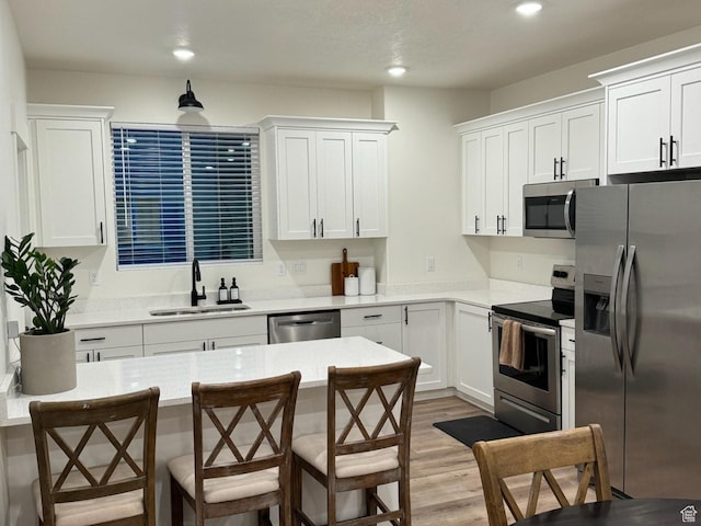 kitchen with a kitchen bar, light wood-type flooring, a sink, white cabinetry, and appliances with stainless steel finishes