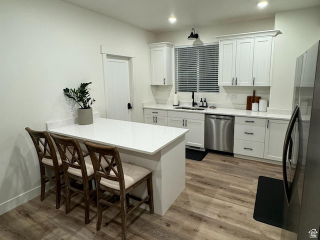 kitchen featuring a sink, a peninsula, light wood-style flooring, and stainless steel appliances