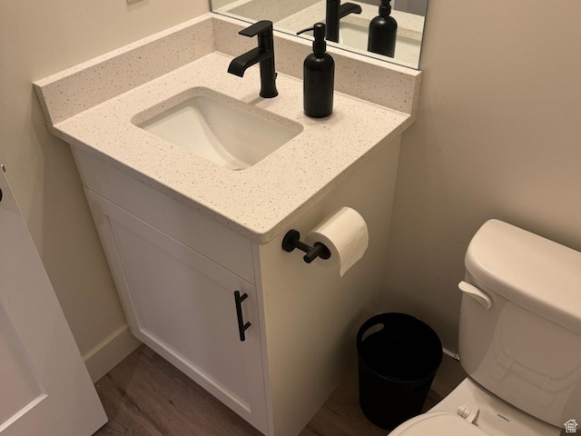 half bath with baseboards, toilet, wood finished floors, and vanity