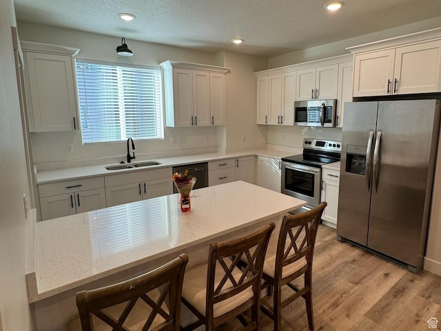 kitchen featuring recessed lighting, a kitchen breakfast bar, appliances with stainless steel finishes, light wood-style floors, and a sink