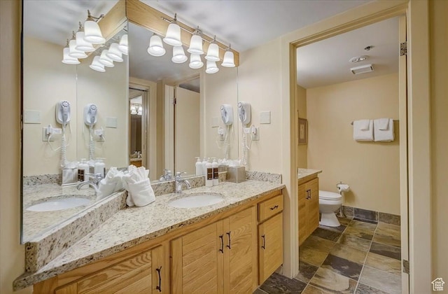 full bath with stone finish floor, vanity, toilet, and baseboards