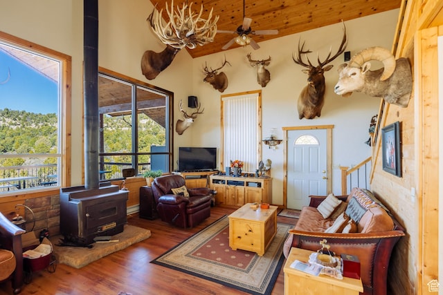 living room featuring ceiling fan, wood-type flooring, a towering ceiling, and a wood stove