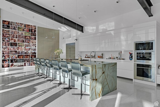 kitchen with beamed ceiling, a breakfast bar area, white cabinets, a large island with sink, and hanging light fixtures