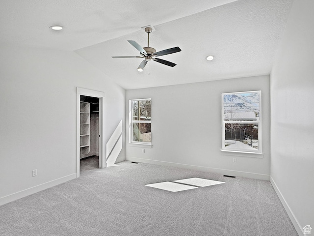 unfurnished bedroom with baseboards, vaulted ceiling, carpet flooring, a walk in closet, and visible vents