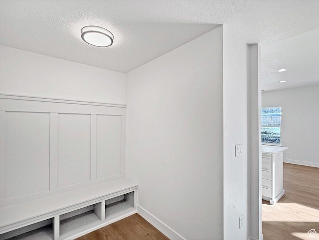 mudroom with a textured ceiling, baseboards, and wood finished floors