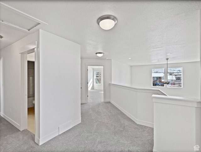 hall featuring an upstairs landing, baseboards, a textured ceiling, and carpet floors