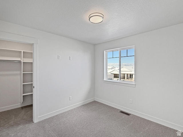 unfurnished bedroom featuring visible vents, a walk in closet, carpet flooring, and a textured ceiling